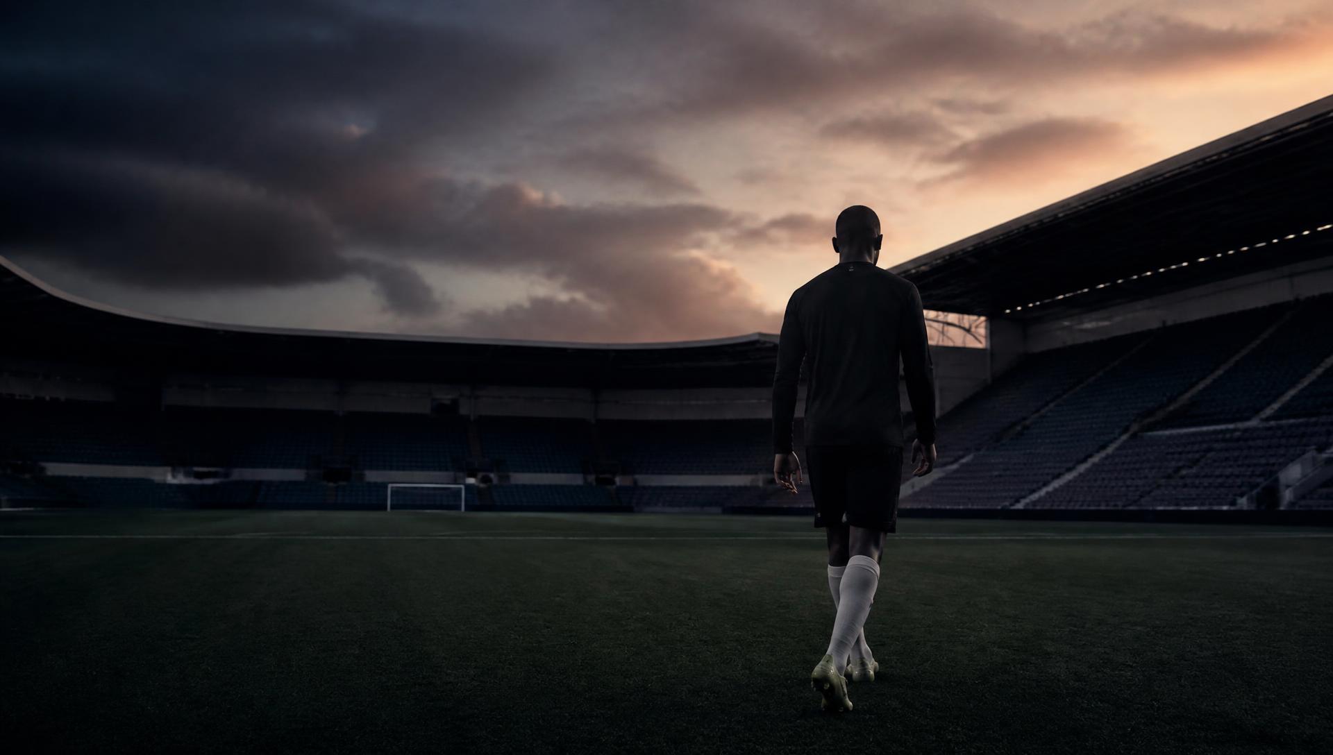 Footballer walking across an empty stadium pitch at dusk